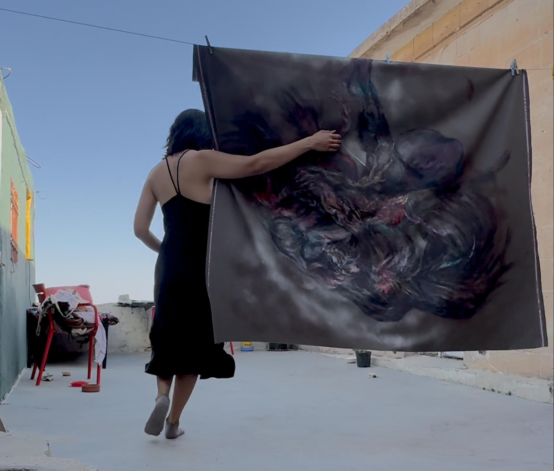 Sinur holding a large painted fabric work outdoors. Sinur holding a large painted fabric work outdoors.